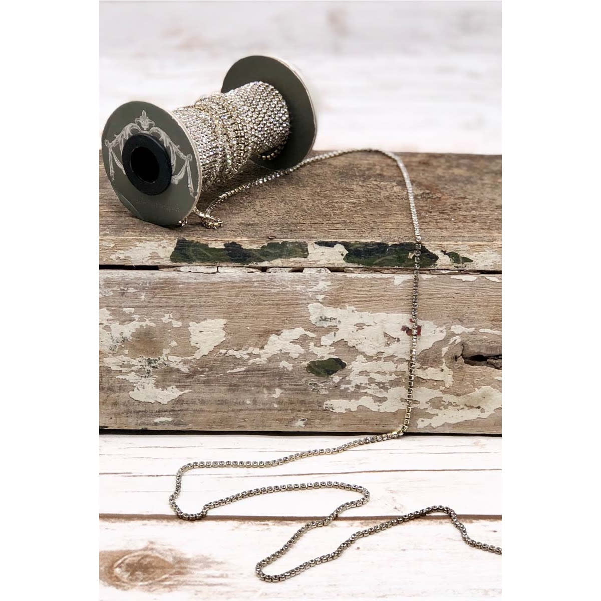A spool of 0.125-inch wide silver-tone iron chain with embedded synthetic quartz crystals.
