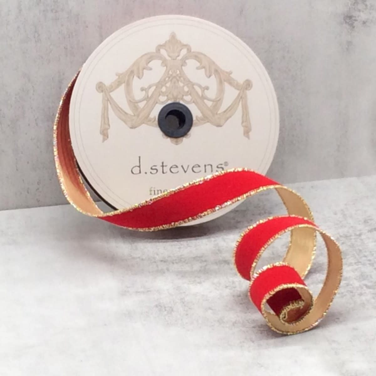 A spool of red flocked velvet ribbon with metallic gold edges on a light gray background.