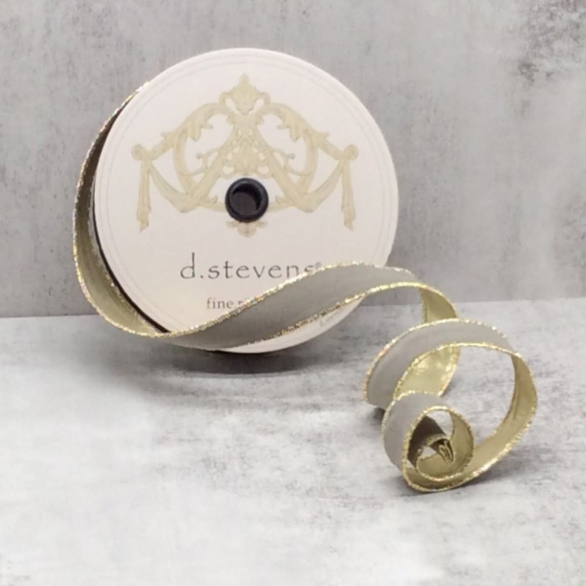 A spool of grey flocked velvet ribbon with metallic gold edges on a light grey surface.