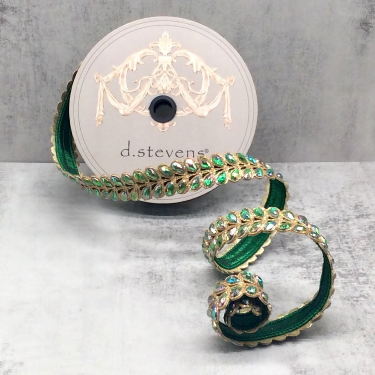 Green ribbon with gold-trimmed, iridescent jewel-encrusted honey locust leaf patterns on a spool.