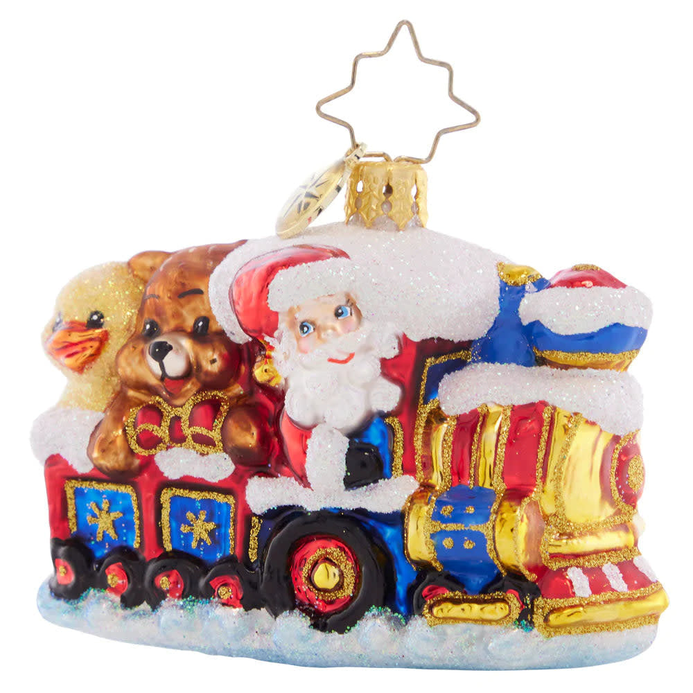 Santa Claus figurine on a red steam train with green accents carrying toys in the snow.