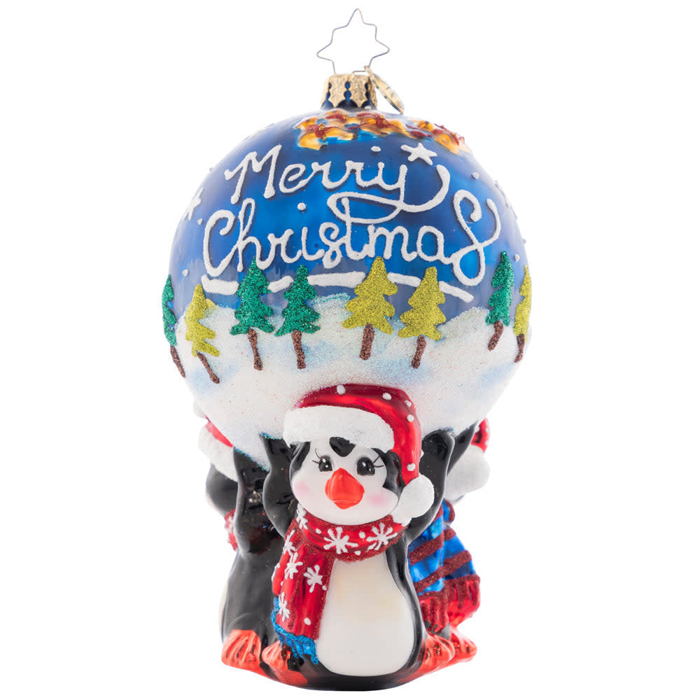 Three penguin figures holding a round ornament featuring Santa flying over snowy trees.