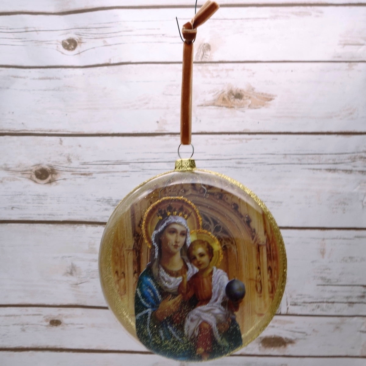 Madonna & Child glass disc ornament with a brown velvet hanger on a white wood background.