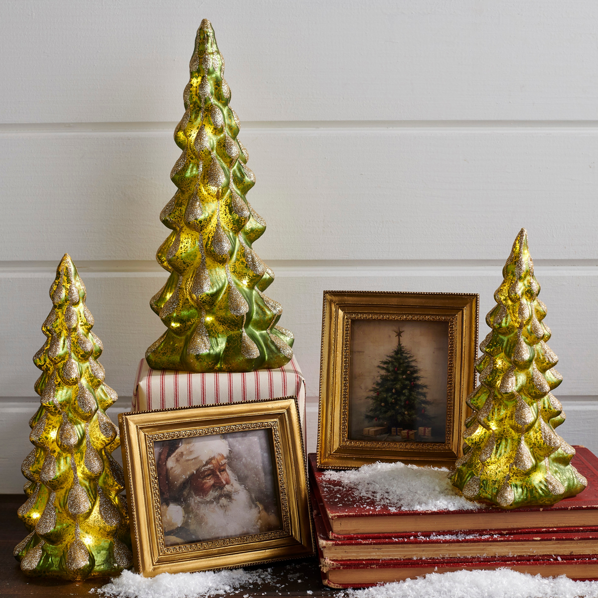 Three lighted green glass Christmas trees with glittery snow accents on a holiday display.
