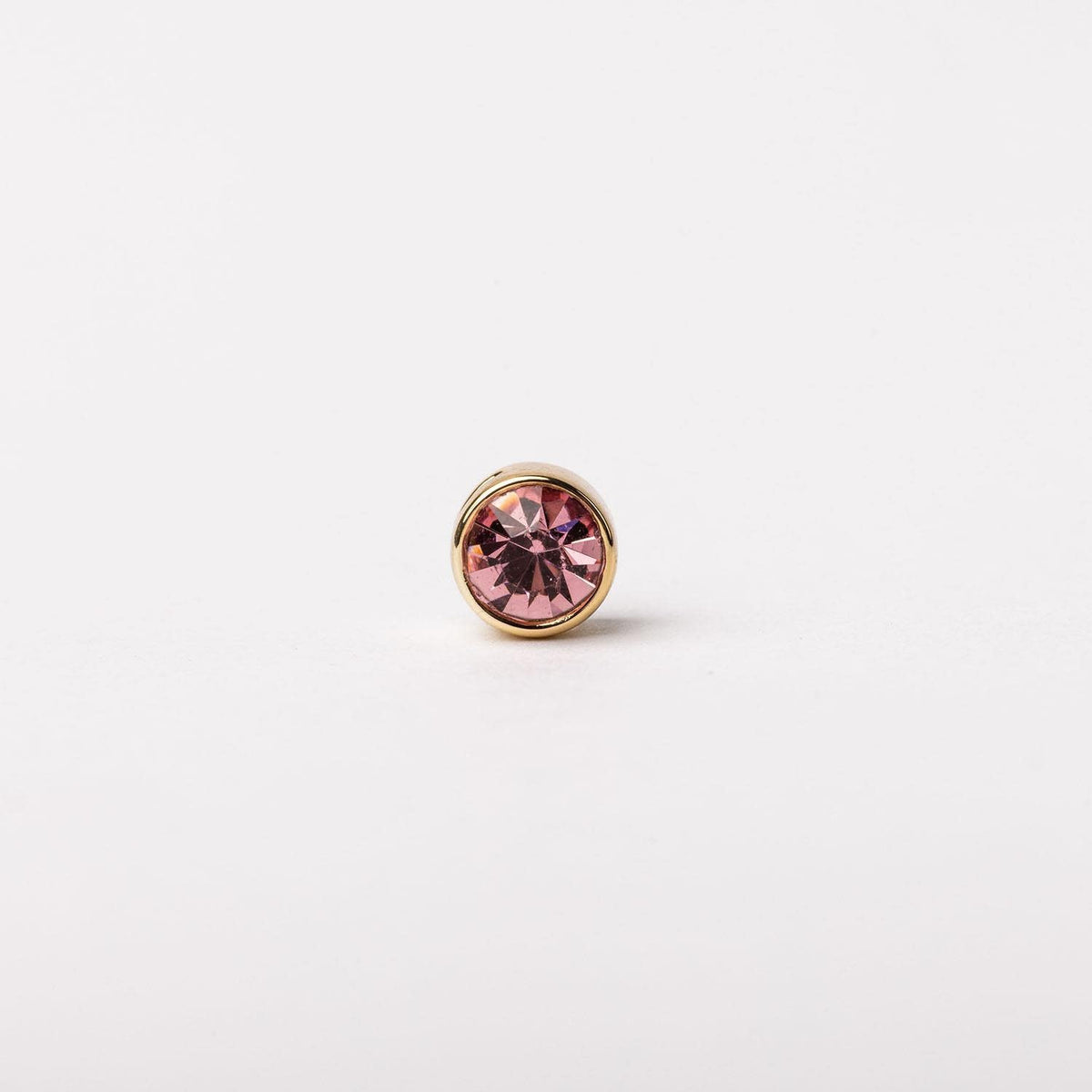 A round gold stud earring featuring a faceted pink gemstone in a bezel setting.