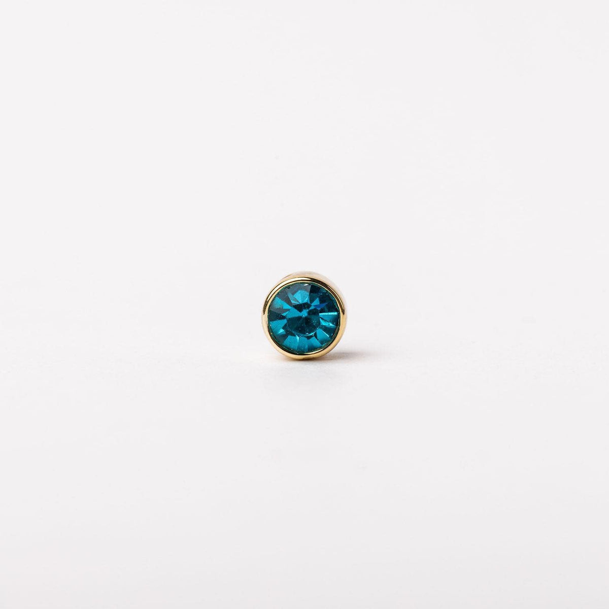 Gold-tone stud earring featuring a round, vibrant blue crystal gemstone in a bezel setting.