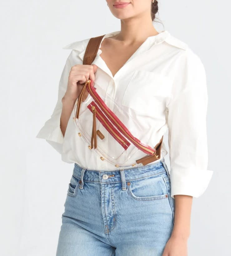 Clear stadium bag with warm brown pebbled leather trim, brushed gold hardware, and red zipper.