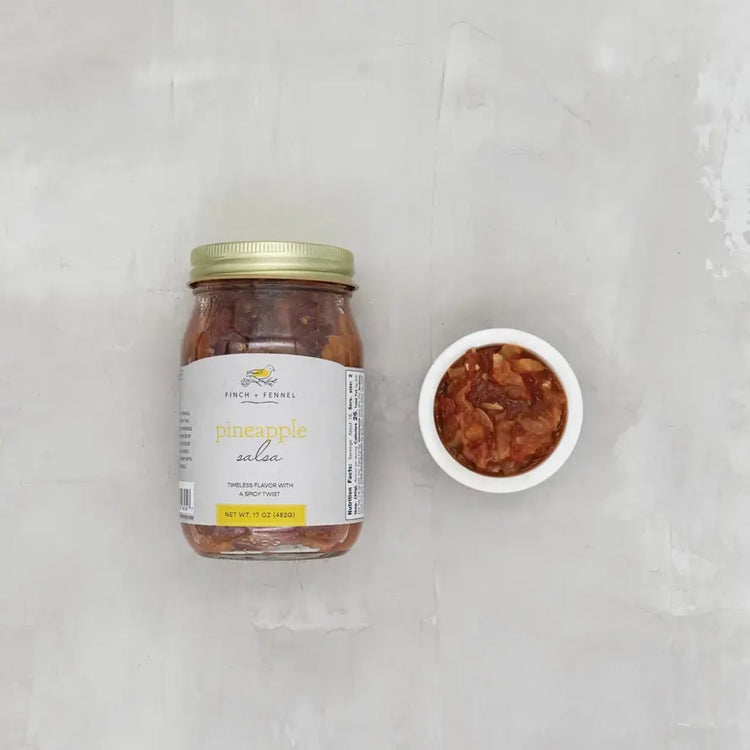 Open jar of pineapple salsa with visible red onion pieces inside a clear glass container.