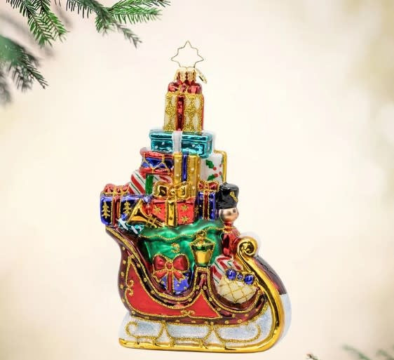 Ornament shaped as Santa's sleigh pulled by reindeer with shimmering festive decorations and overflowing gifts.