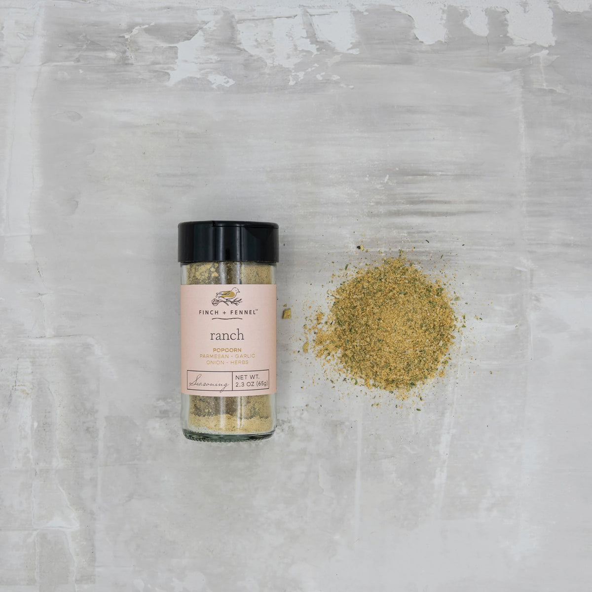 Finch + Fennel Ranch Popcorn Seasoning in a 2.3 oz glass jar next to a pile of the seasoning.