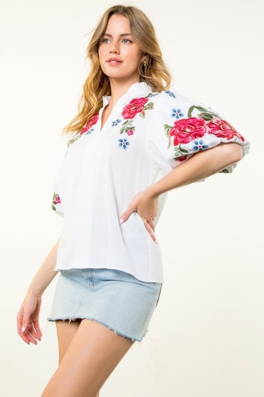 A white blouse with colorful floral embroidery, puff sleeves, and a V-neckline.