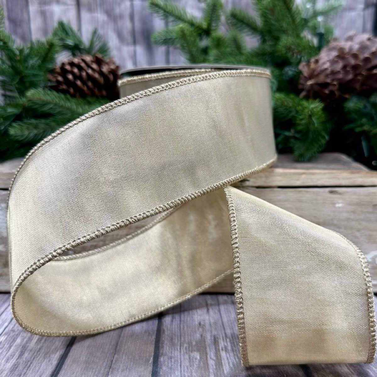 A roll of 2.5-inch wide metallic gold mesh ribbon with a finished edge on a rustic wooden surface.
