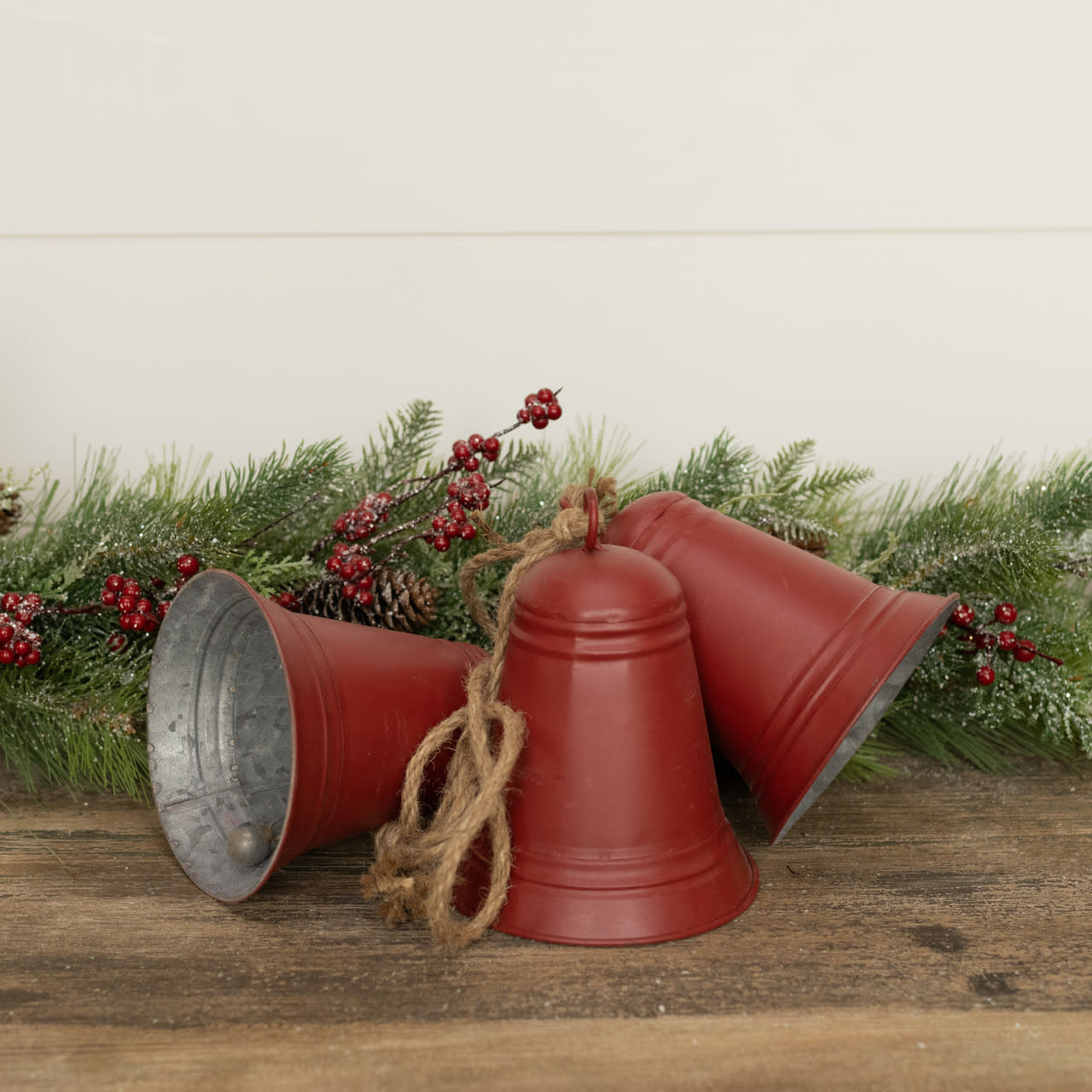 Three red metal bells tied together with rustic twine, resting on a wooden surface with greenery.