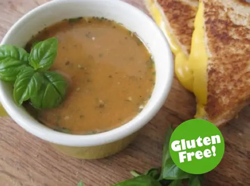 A bowl of creamy soup garnished with fresh basil next to a grilled cheese sandwich.