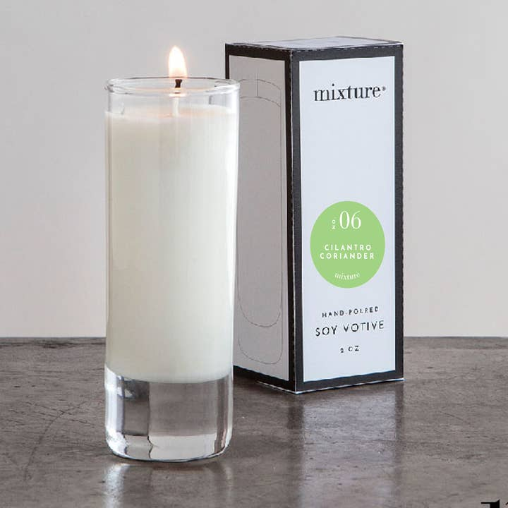 A lit 2 oz clear glass cylinder votive candle next to its white and black branded box.