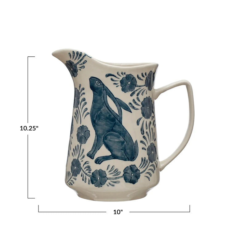 Cream stoneware pitcher with a blue hand-painted rabbit and floral pattern, 10.25 inches tall.