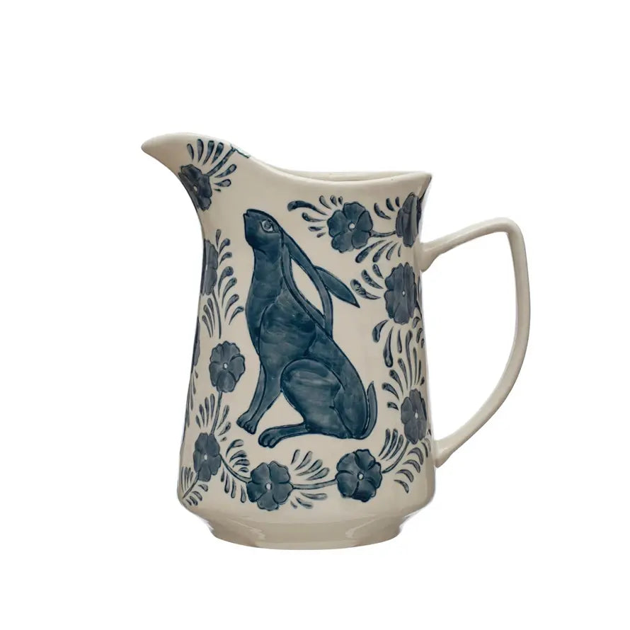Cream stoneware pitcher with hand-painted blue rabbit and floral patterns.