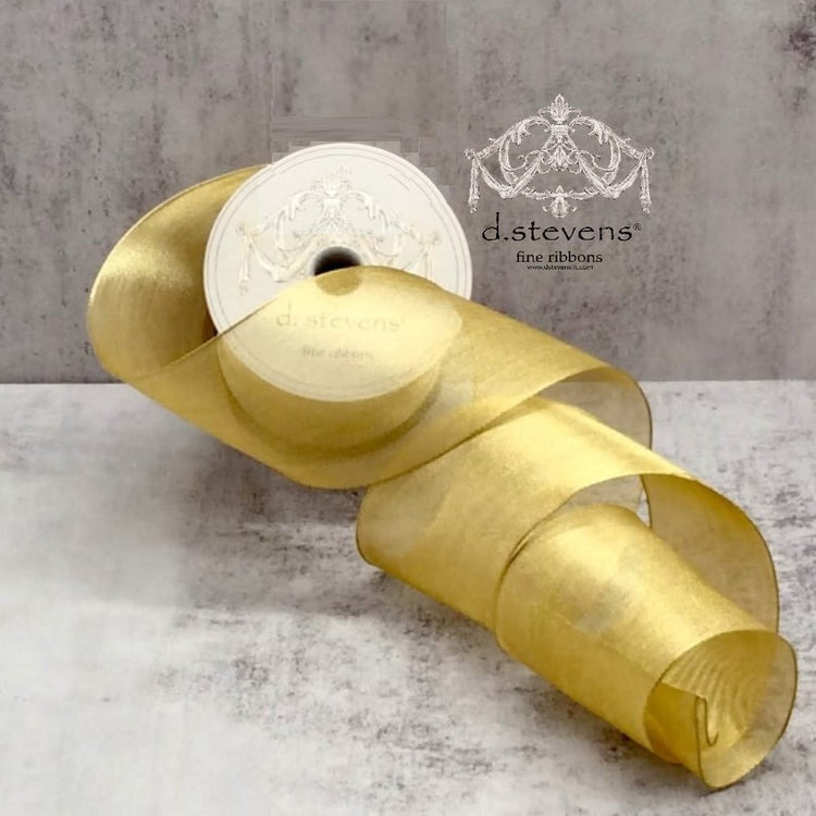 A roll of gold metallic mesh ribbon by d.stevens on a textured gray background.