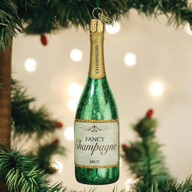 Glass champagne bottle ornament with gold foil accents on a clear stand.