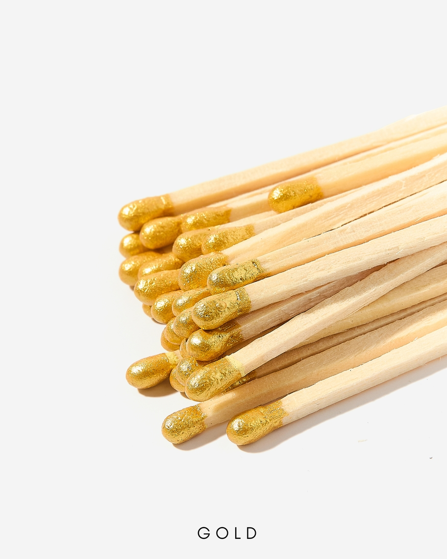 A bundle of 3-inch wooden safety matches with metallic gold tips against a white background.