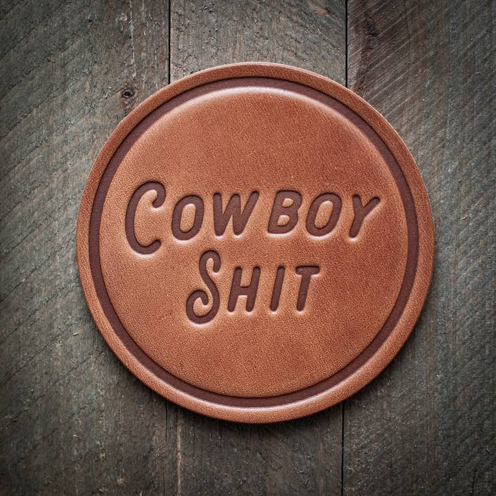 Square brown leather coaster with a cowboy print featuring black boots and hats.