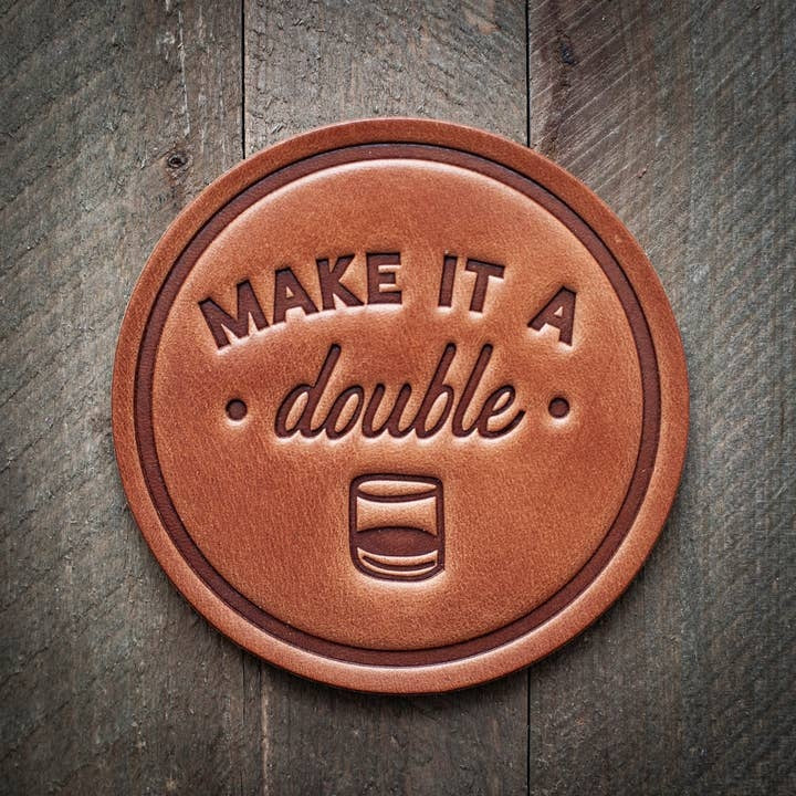 Four square leather coasters in tan with visible stitching arranged on a surface.