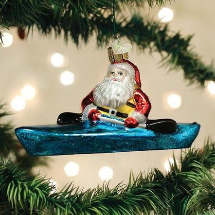 Mouth-blown glass Santa ornament in a kayak with silver accents and hand-painted glitter finish.