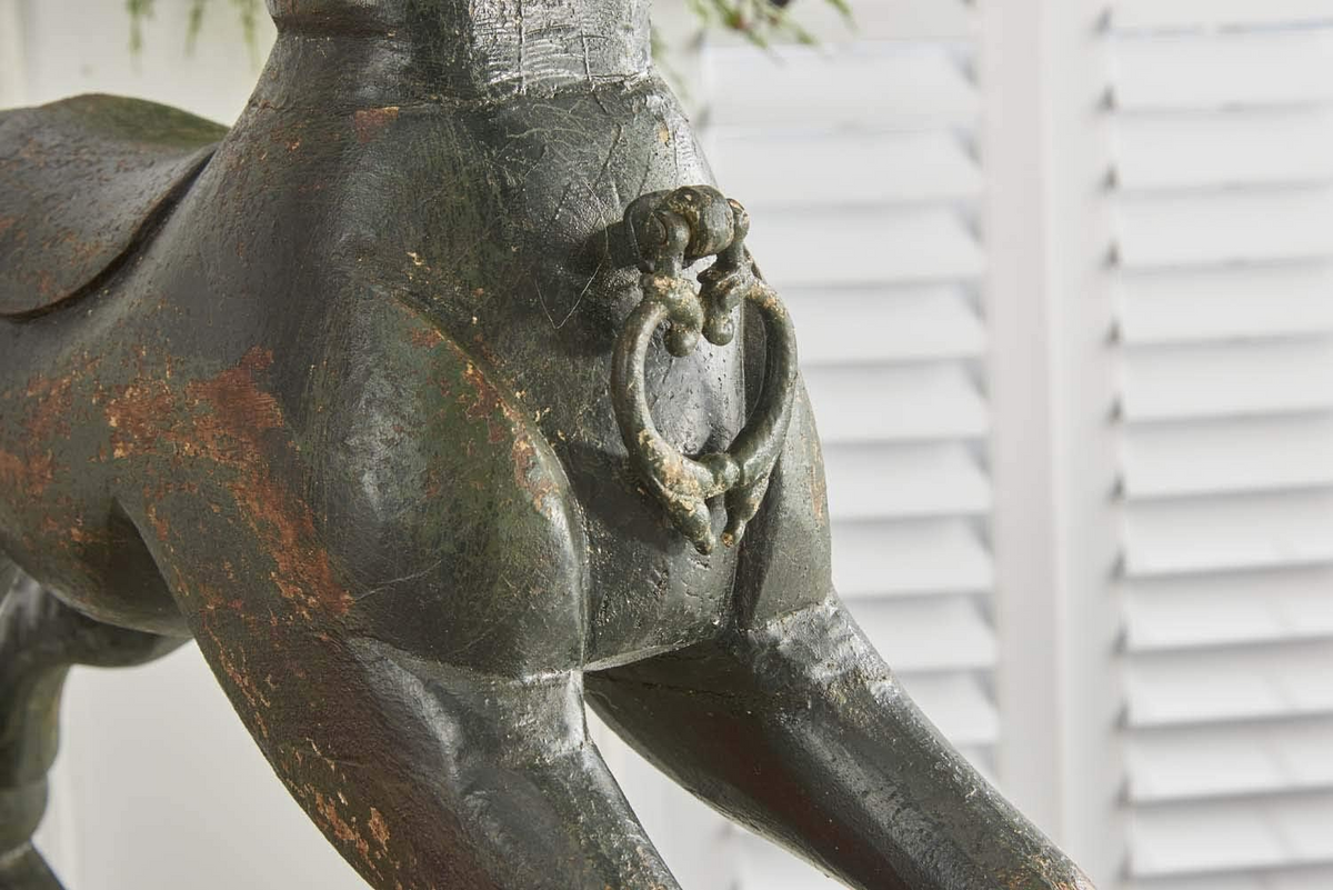 Close-up of a black painted wooden rocking horse featuring a metal ring handle and weathered finish.