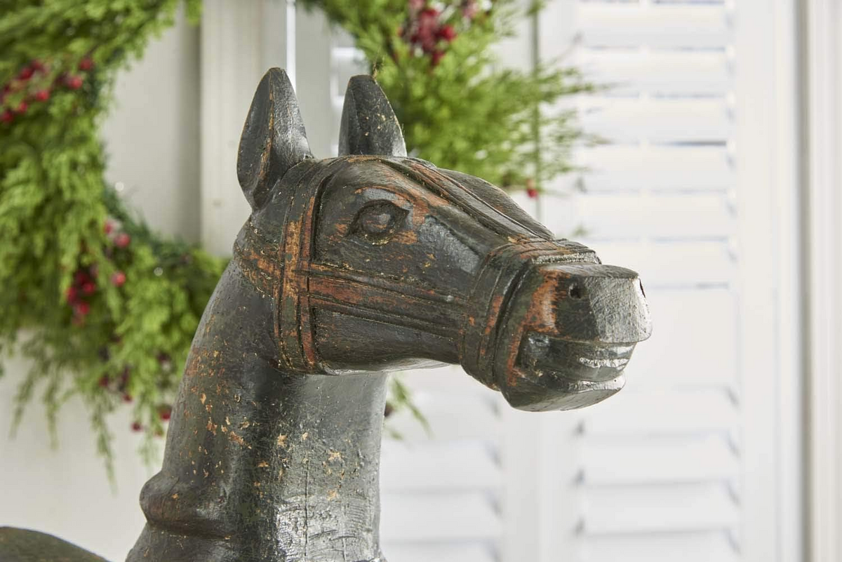 Close-up of a black painted wooden rocking horse head with carved harness details.