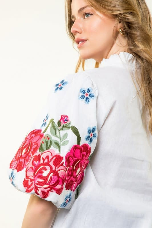 White blouse with puff sleeves featuring vibrant pink floral and blue flower embroidery.
