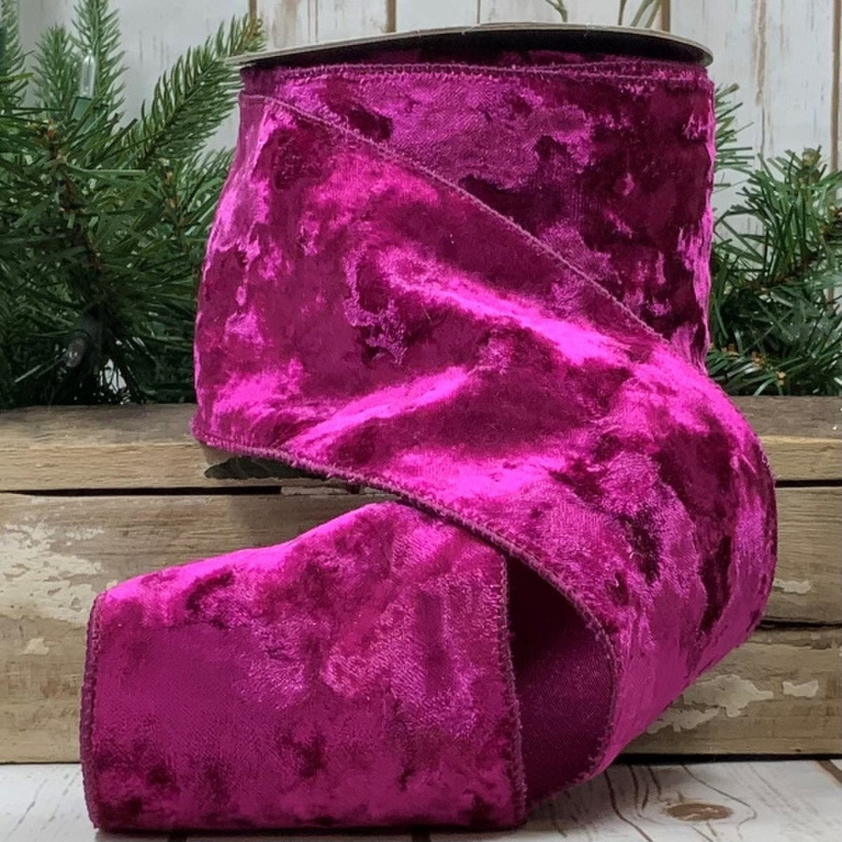 4 inch wide fuchsia crushed velvet ribbon on a spool, displayed against a rustic wooden background.