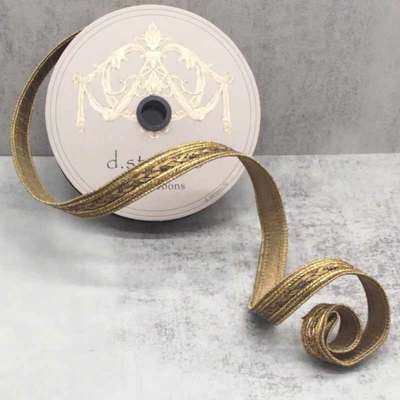 0.5 inch antique gold metallic braid wired trim ribbon unspooled on a gray surface.