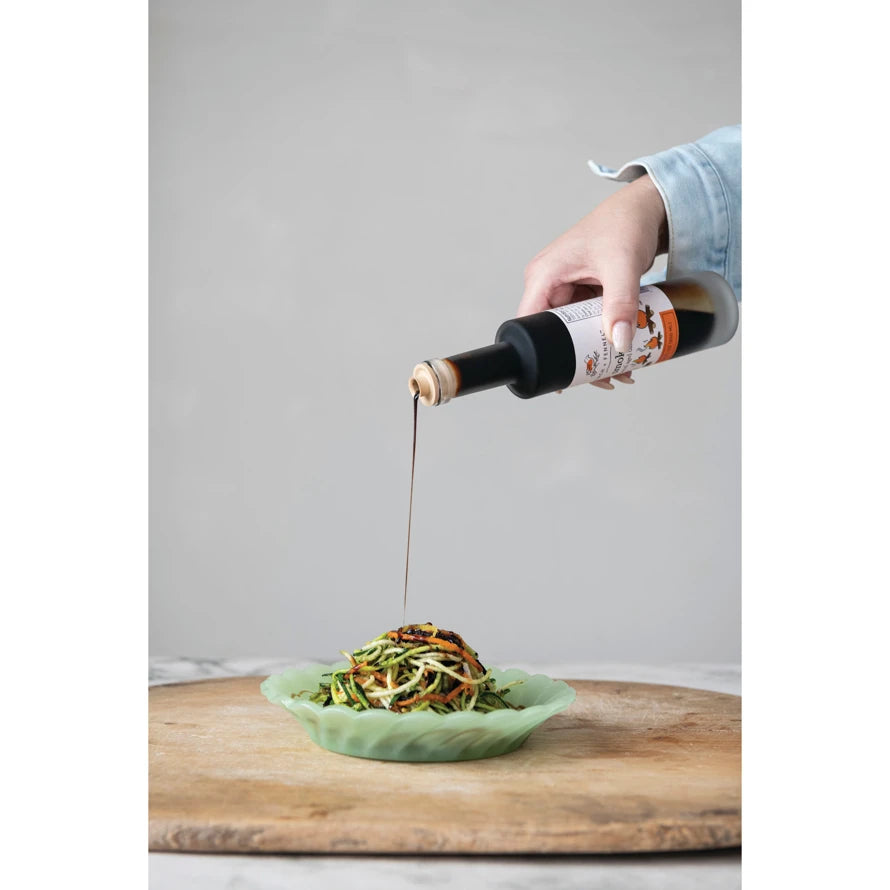 A person pouring 6.8 oz. Bourbon Barrel Aged Balsamic vinegar over a bowl of zucchini noodles.