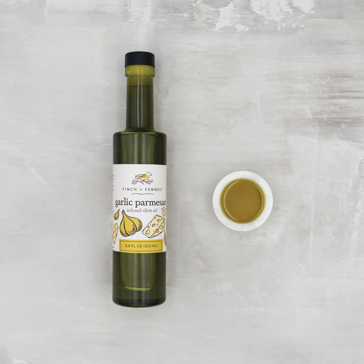 6.8 oz. Garlic Parmesan Infused Olive Oil bottle next to a small white bowl of oil.