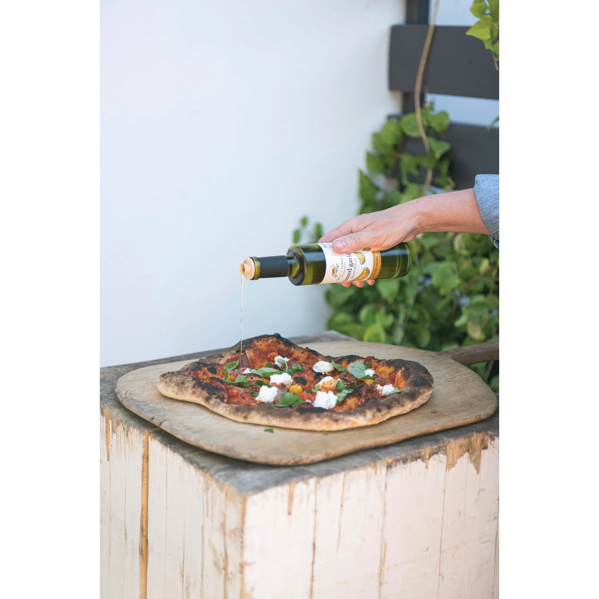 A person pours Garlic Parmesan Infused Olive Oil from a 6.8 oz bottle onto a fresh artisan pizza.