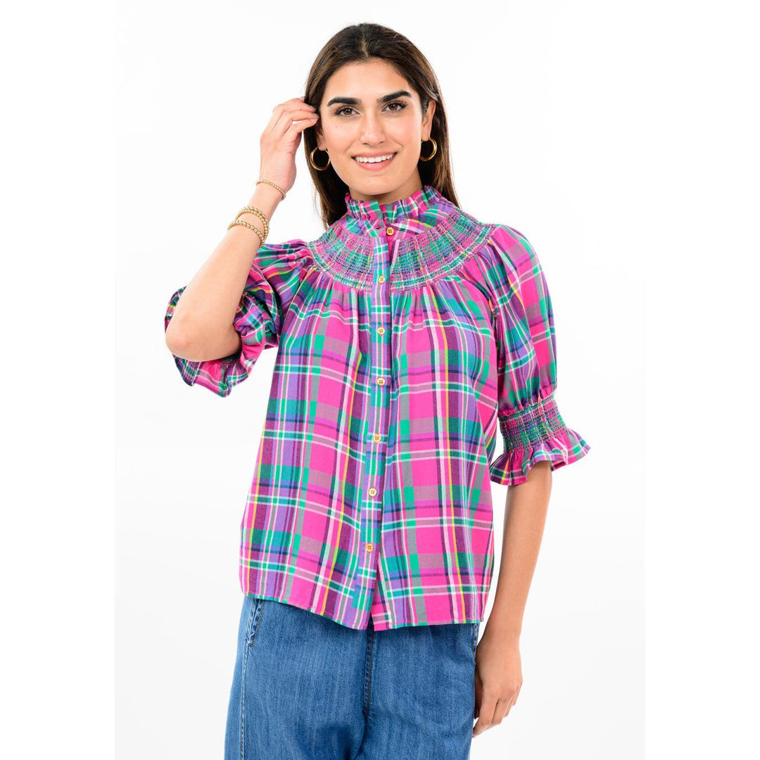 Woman wearing the Ava Plaid Smocked Yoke Blouse in pink and green plaid with blue jeans.
