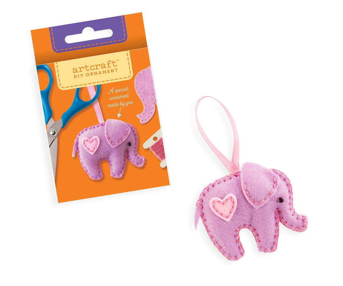 DIY Felt Ornament Kit with red felt pieces, batting, thread, needles, pom poms, and ribbon arranged on a white surface.