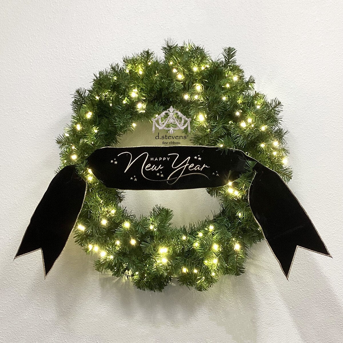 Black velvet ribbon with gold embroidered Happy New Year text on a lit green wreath.