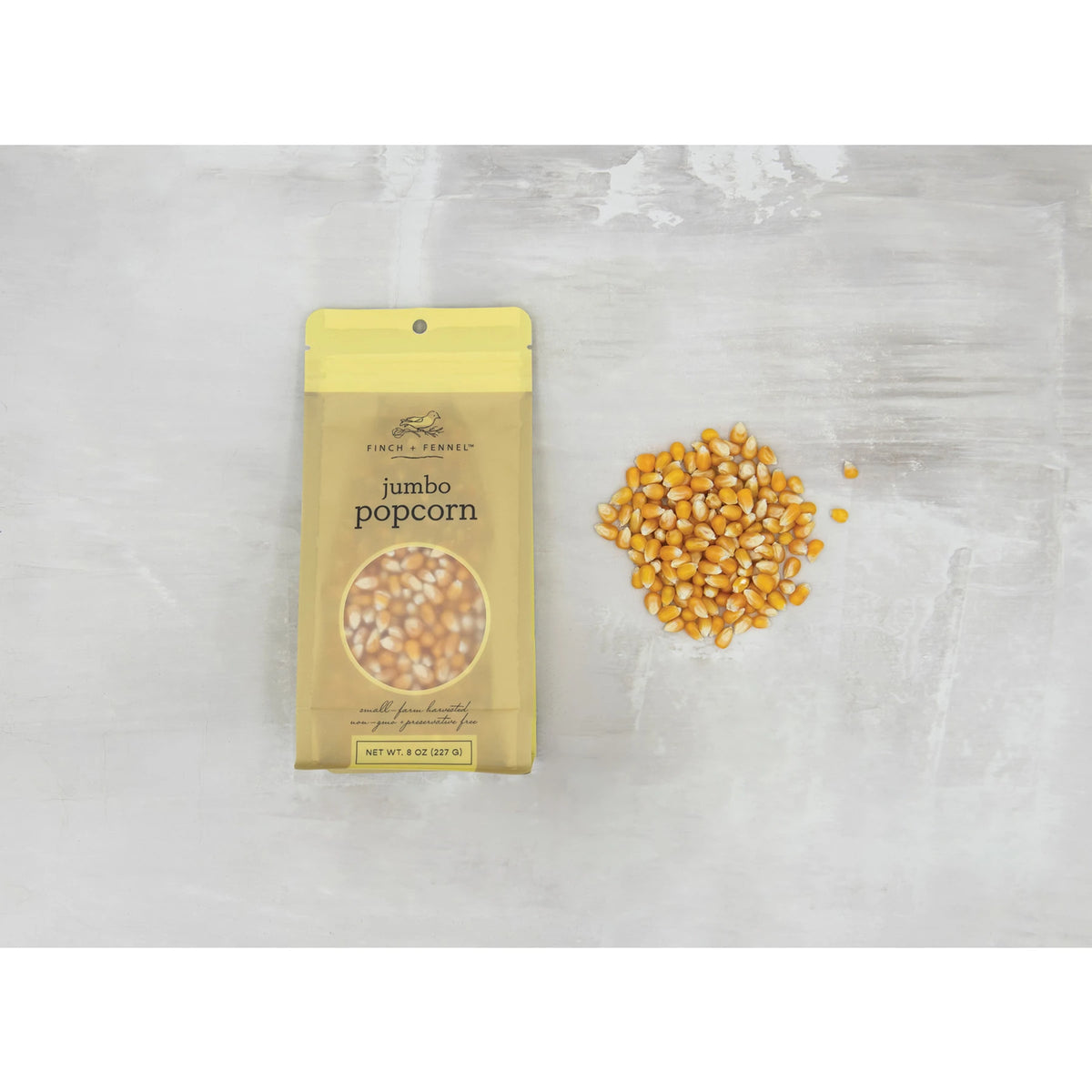 8 oz. bag of Finch + Fennel Jumbo Popcorn next to a pile of loose yellow corn kernels.