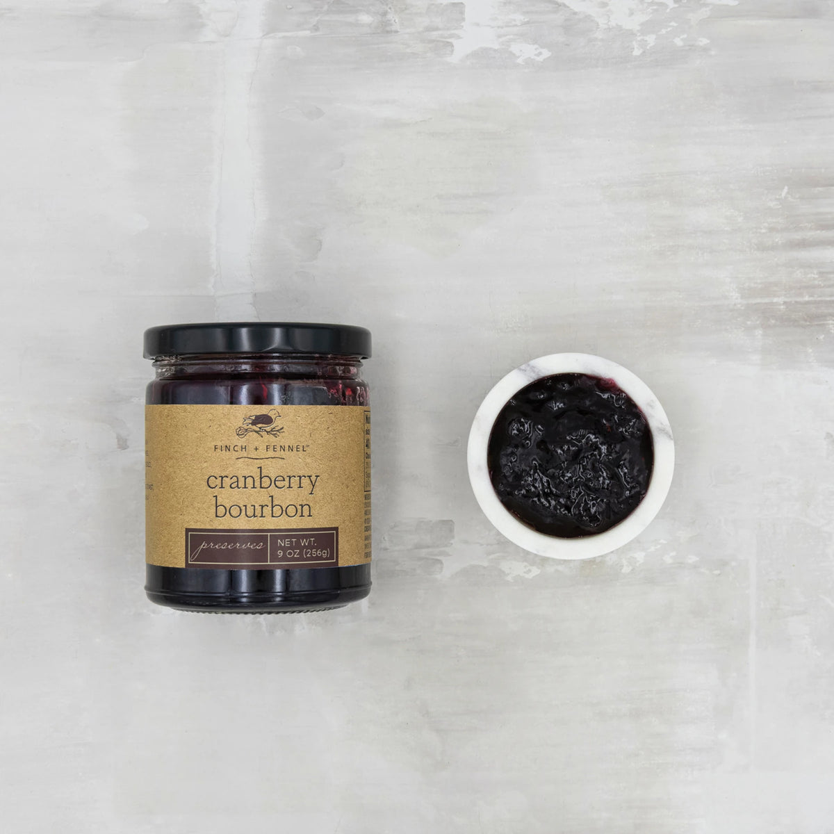 A jar of Finch + Fennel Cranberry Bourbon Preserves next to a small bowl of the dark fruit spread.