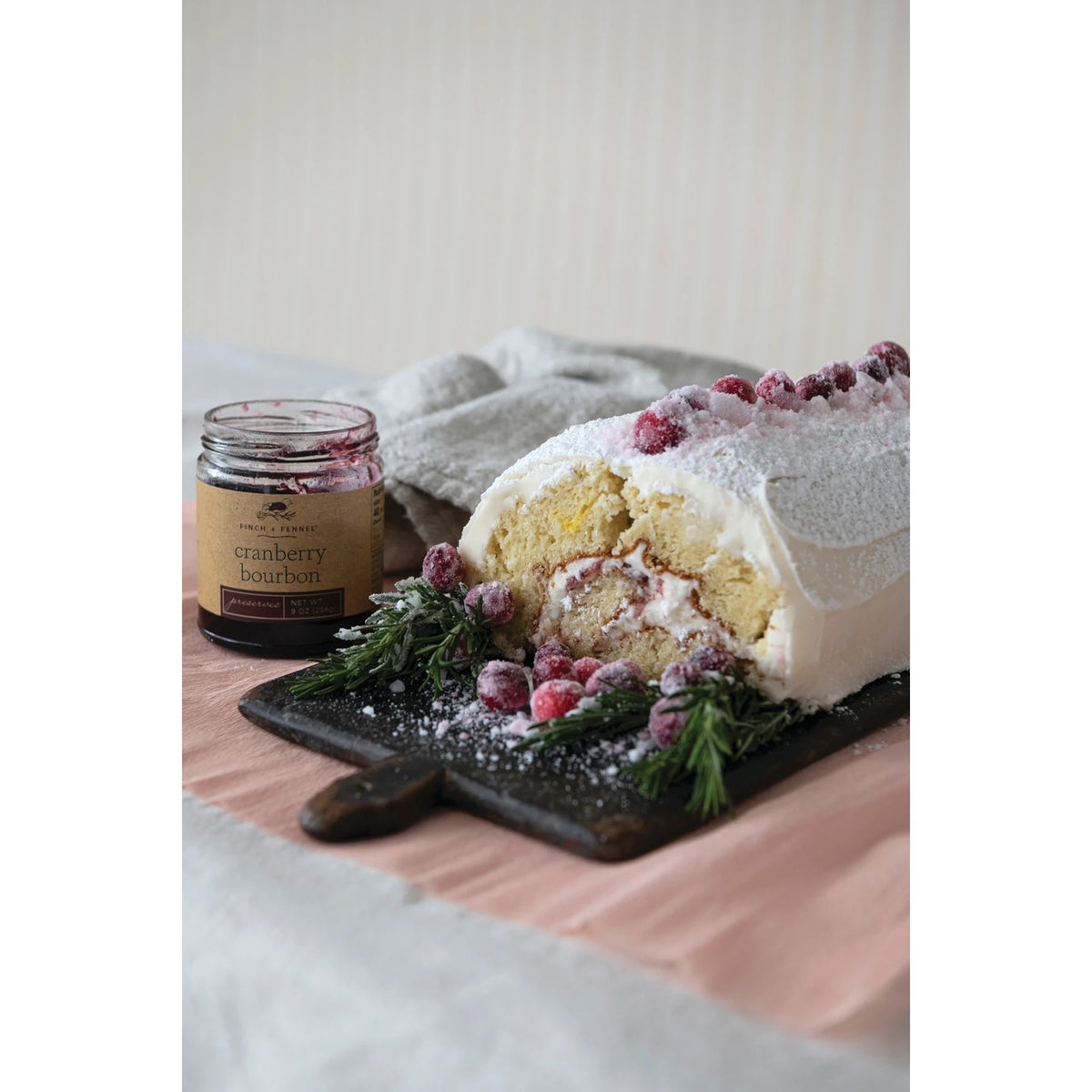 9 oz. jar of Cranberry Bourbon Preserves next to a frosted cake roll with sugared cranberries.