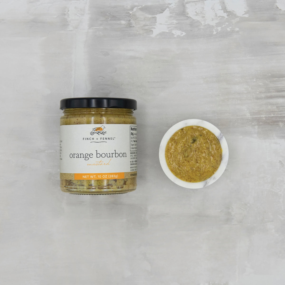 A jar of Finch + Fennel Orange Bourbon Mustard next to a small marble bowl of the mustard.