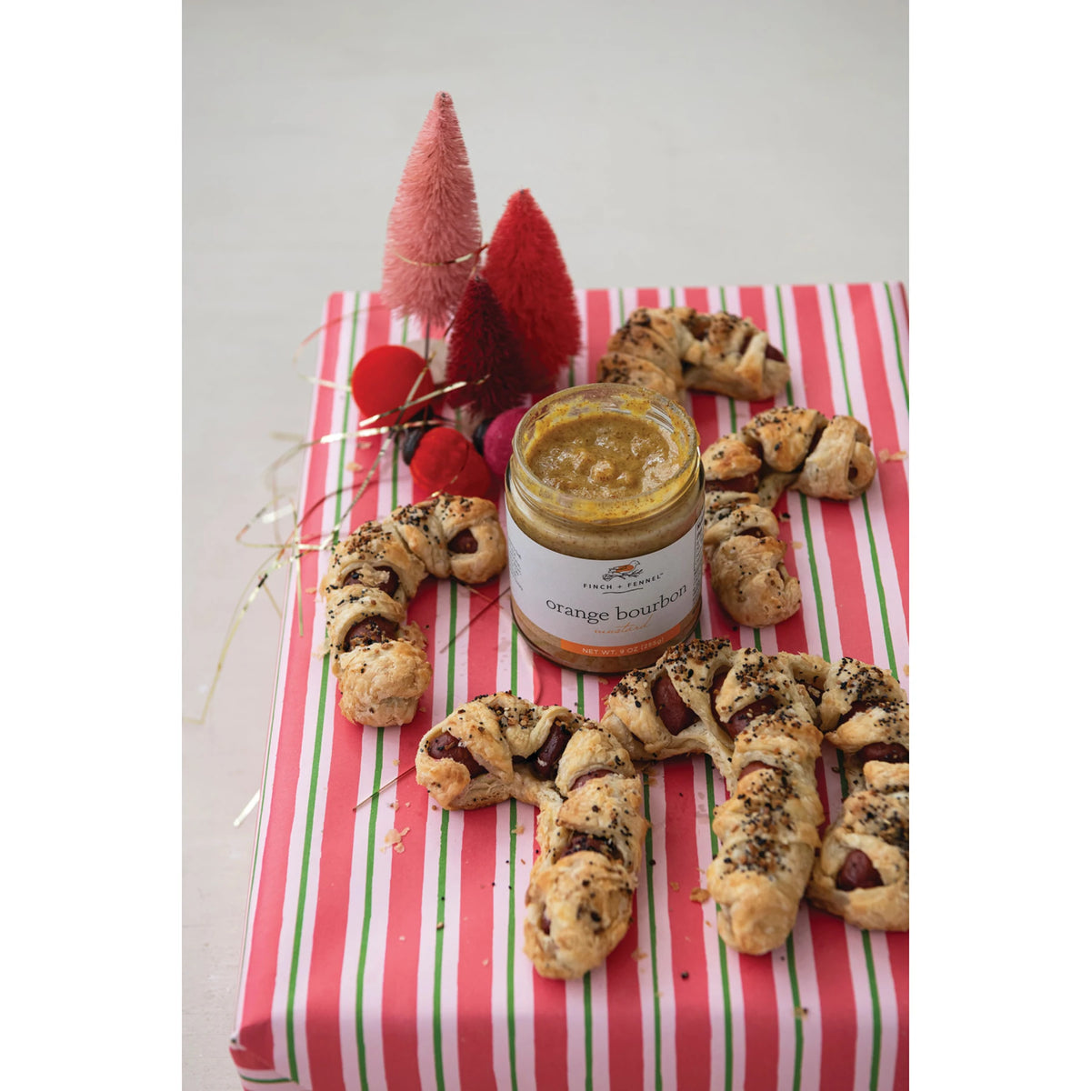 A jar of Finch + Fennel Orange Bourbon Mustard surrounded by puff pastry appetizers.