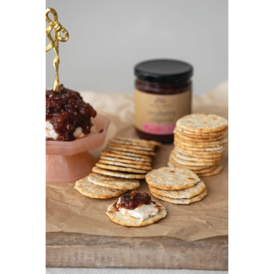 9 oz. Raspberry Chipotle Jam jar next to a stack of crackers and a cracker topped with jam.