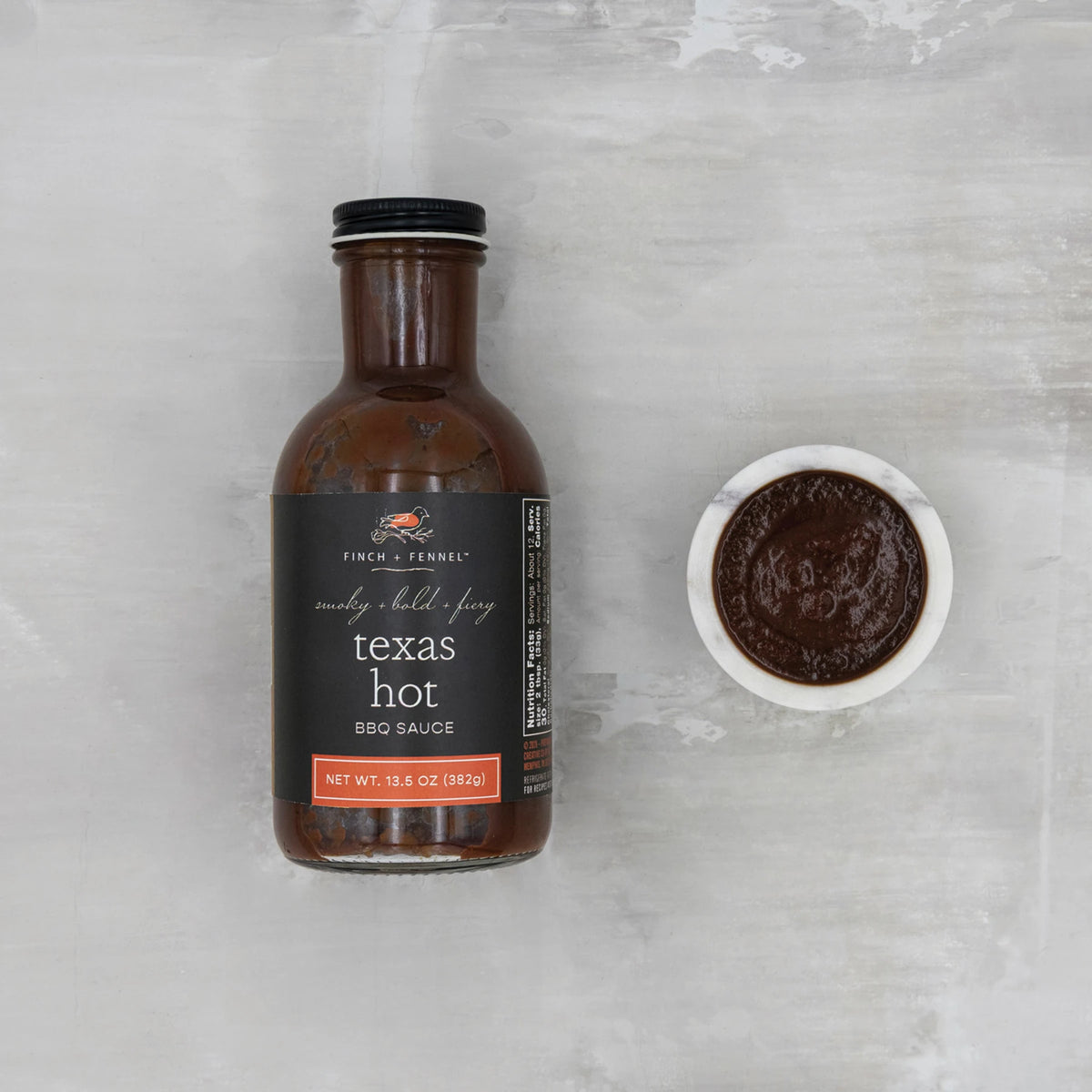 A bottle of Finch + Fennel Texas Hot BBQ Sauce next to a small bowl of the dark brown sauce.