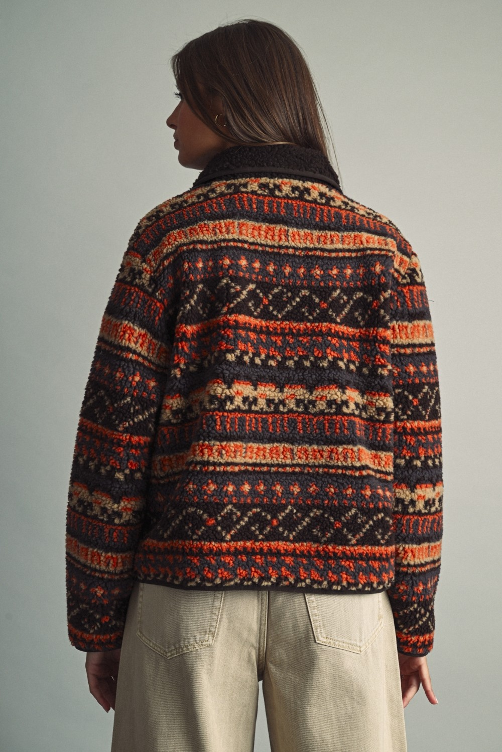 Back view of a woman in an ethnic patterned teddy fleece jacket in rust, beige, and dark brown.
