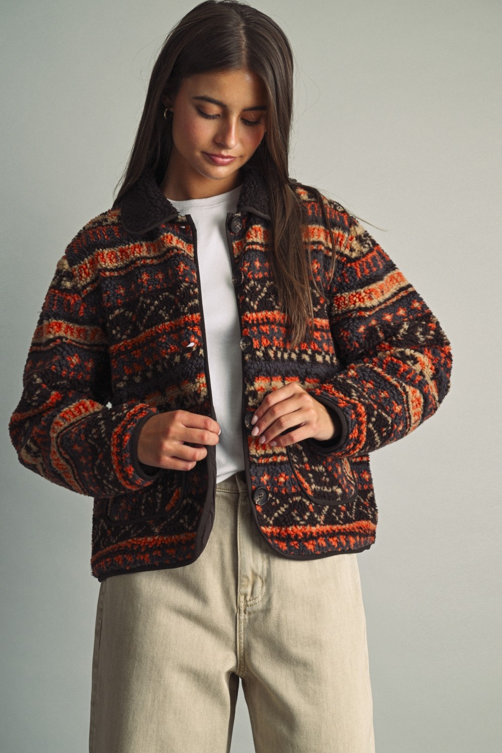 Woman wearing a Camila ethnic patterned teddy fleece jacket in rust and brown with beige pants.