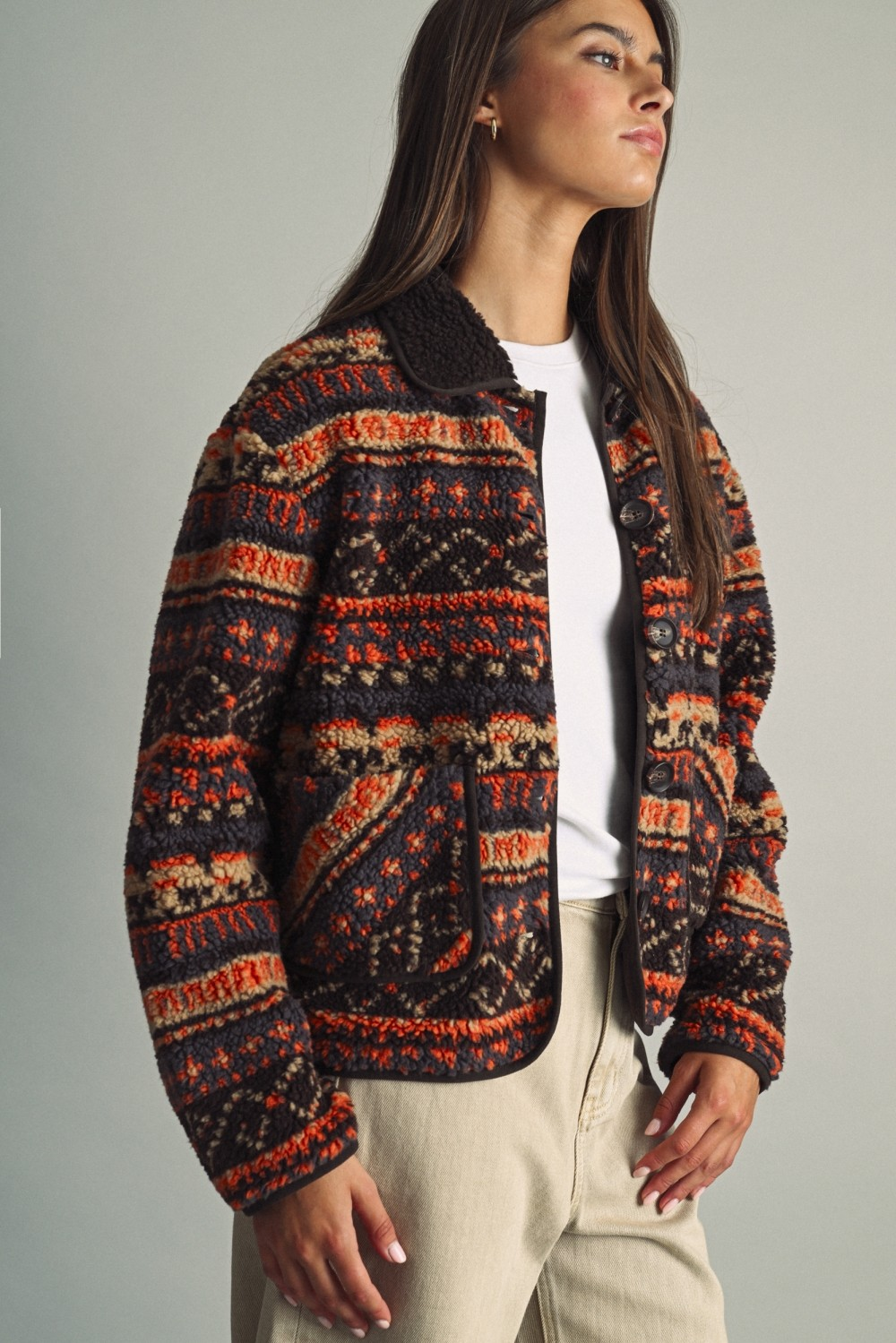 Woman wearing a Camila ethnic patterned teddy fleece jacket in rust and brown with beige pants.