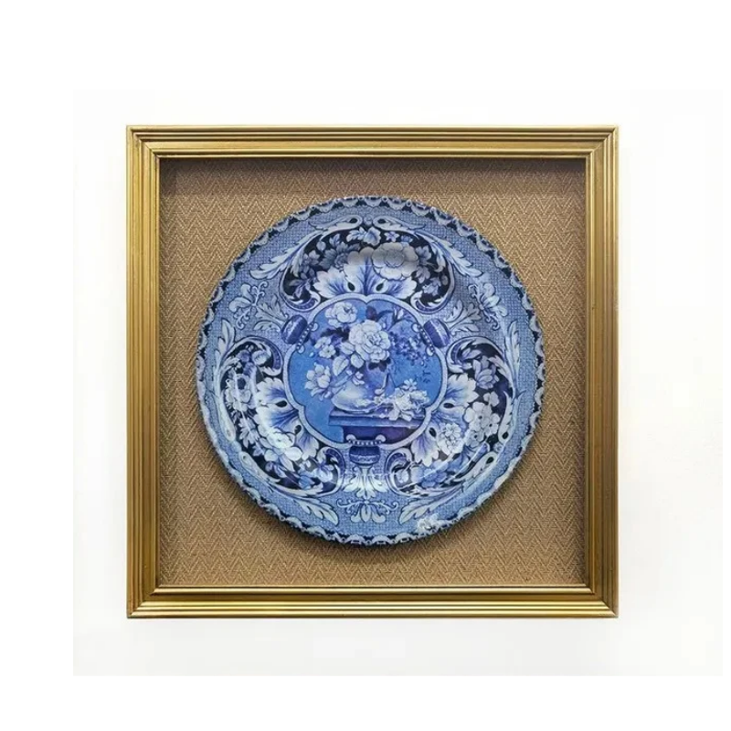 Framed print of a blue and white floral plate in a gold frame with a textured tan background.