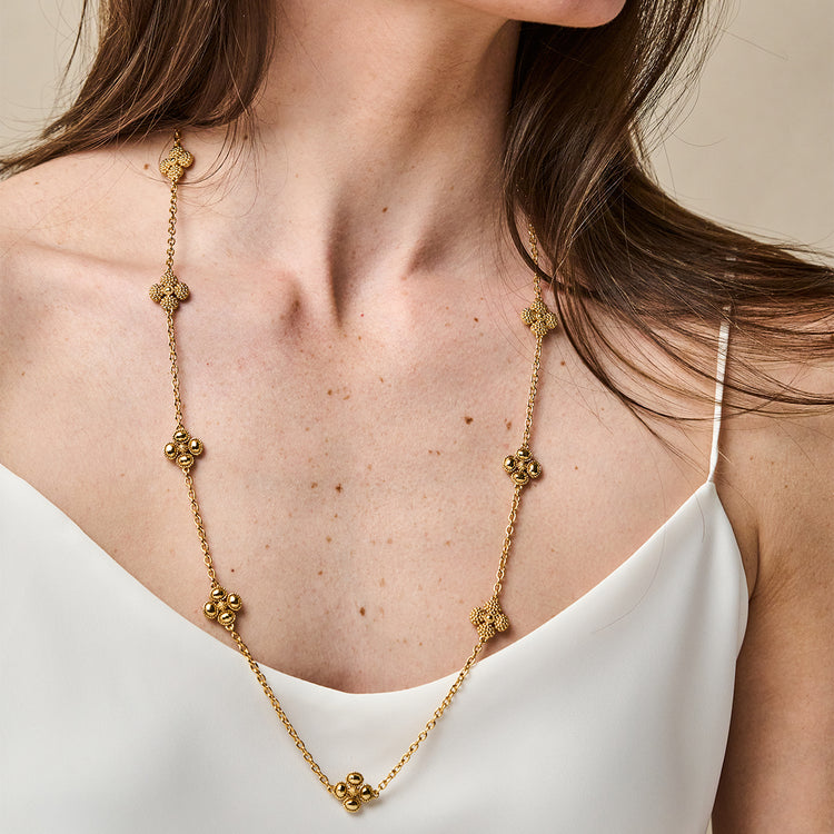 Woman wearing a 28-inch gold chain necklace with station-set textured clover motifs.
